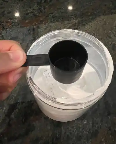 a measuring spoon full of powder over a jar. The jar appears to be filled with protein powder.