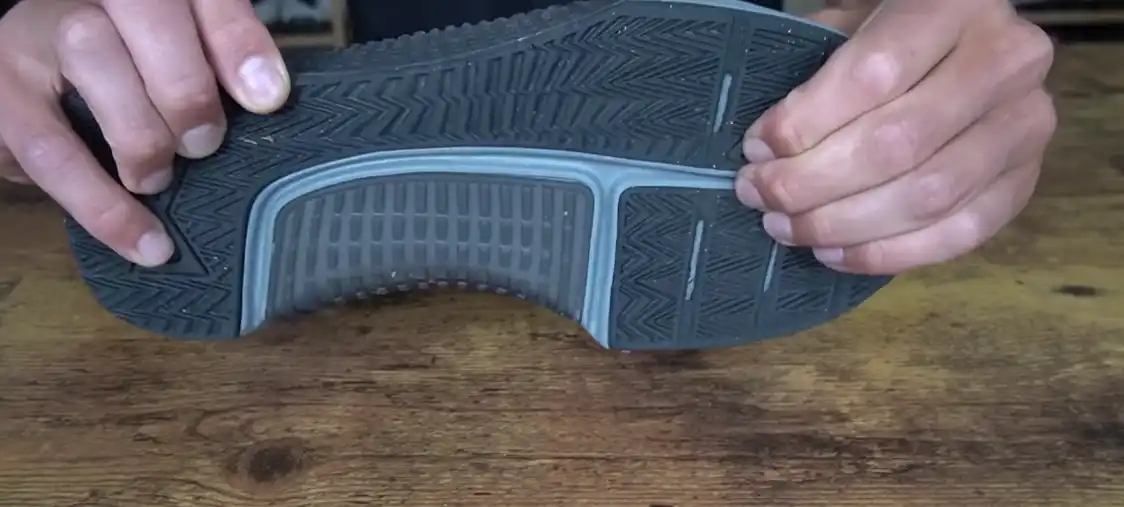 Close-up of hand holding a nike metcon 9 black sole on a wooden table.