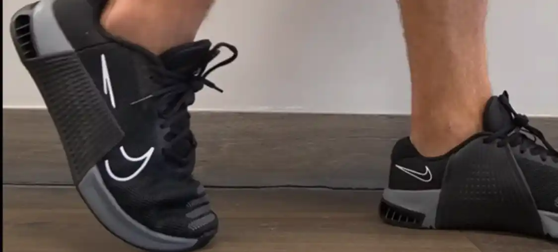 Close-up of a black Nike shoe with a gray swoosh doing calf one-leg exercise on a wooden floor.