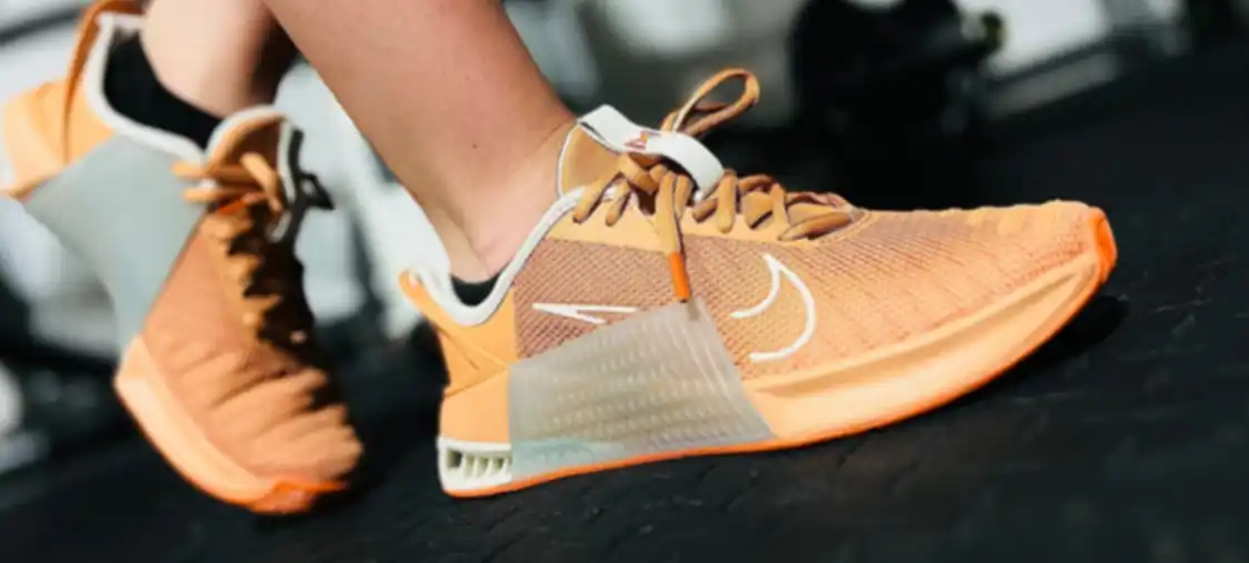 A close-up of orange and white Nike Metcon 9 running shoes on a treadmill.