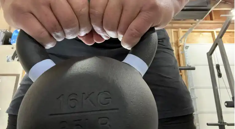 A man in a garage holding a onnit kettlebell with the weight 16kg labelled on it.