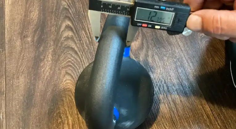  a person measuring the diameter of a kettlebell handle with a digital caliper. 